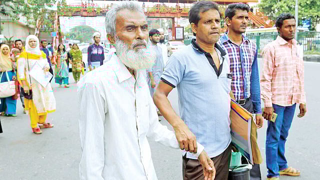 ক্যানসারের রোগী সুলতান মিয়াকে (বাঁয়ে) নিয়ে মহাখালীর ক্যানসার হাসপাতালে যেতে প্রায় এক ঘণ্টা শাহবাগ মোড়ে বাসের অপেক্ষায় দাঁড়িয়ে ছিলেন হারুন উর রশিদ। এ সময় বাসের অপেক্ষায় আরও অনেকেই সেখানে দাঁড়িয়ে ছিলেন। ছবিটি গতকাল দুপুরে তোলা l আবদুস সালাম