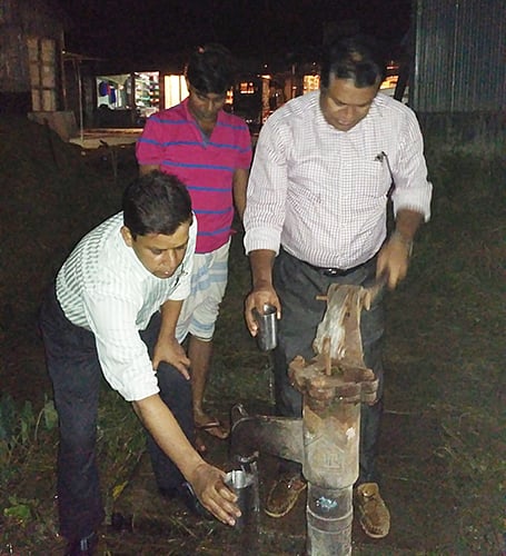 টিউবওয়েল থেকে সংগ্রহ করা পানি পাশের একটি চায়ের দোকানে বসে বিভিন্ন যন্ত্রের মাধ্যমে পরীক্ষা করছেন দুই কর্মকর্তা। ছবি: প্রথম আলো