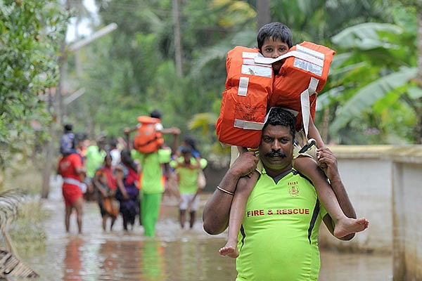 লাইফ জ্যাকেট পরিয়ে শিশুটিকে উদ্ধার করে নিয়ে যাচ্ছেন ফায়ার সার্ভিসের এক কর্মী। ত্রিশুর, কেরালা, ভারত, ১৯ আগস্ট। ছবি: এএফপি