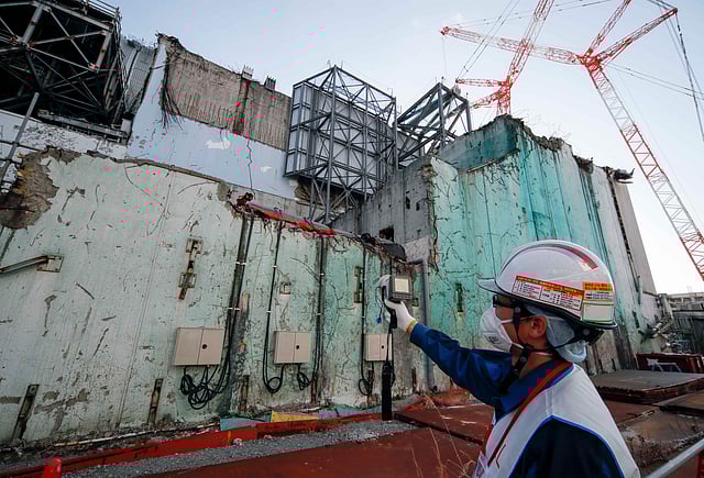 বিধ্বস্ত চুল্লি ভবনের বাইরে তেজস্ক্রিয়তার মাত্রা পরিমাপ করছেন টেপকো কর্মী। ছবি: কিমিমাসা মাইয়ামা