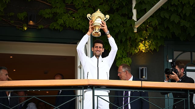 অল ইংল্যান্ড ক্লাবের ক্লাব হাউসে শিরোপা হাতে জোকোভিচ। ছবি: এএফপি