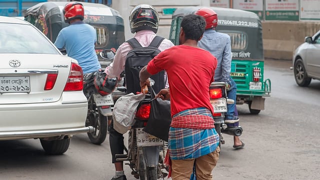 সার্ক ফোয়ারার মোড়ে মোটরসাইকেলের পেছনের ব্যাগ কাটার চেষ্টা করছে যুবকটি। ছবি: সাজিদ হোসেন