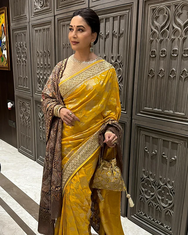 জমকালো জারদৌসি কাজের পাড়ের শর্ষে হলুদ ফুলেল প্যাটার্নের শাড়ির সঙ্গে বাদামি শাল নিয়েছেন মাধুরী। হাতে সোনালি বটুয়া।