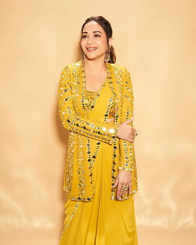 মাধুরীর পরনে ম্যাচিং জ্যাকেটের লেয়ারিং রয়েছে হলুদ শিফনে জমকালো মিরর ওয়ার্কের ম্যাচিং শাড়ি ব্লাউজের ওপরে।