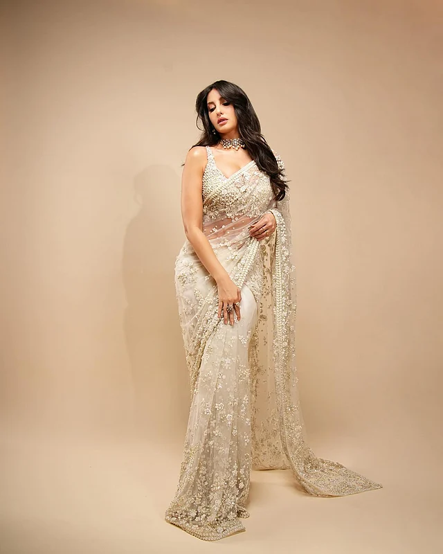 আইভরি শিয়ার ফেব্রিকে কারুকাজ করা শাড়ি পরেছেন নোরা ফাতেহি। স্লিভলেস ব্লাউজে সিকুইনের কাজ।