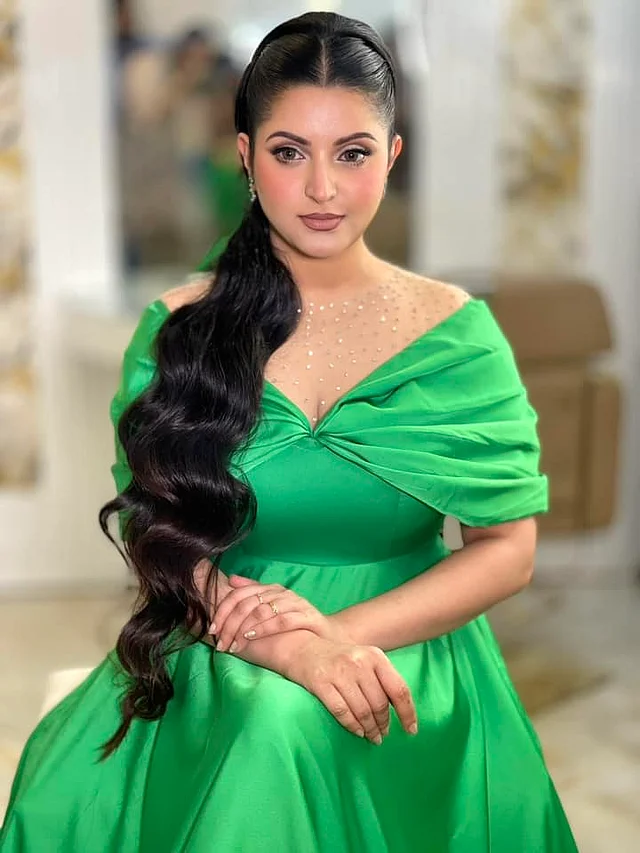 উজ্জ্বল টিয়ে সবুজ গাউনটি মনোক্রোম থিমের। ত্রিকোণাকার আকর্ষণীয় নেকলাইন রাখা হয়েছে এতে। র্যাপ স্লিভস দেখা যাচ্ছে।