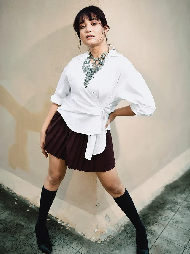 সাদা র্যাপ শার্টের সঙ্গে প্লিটেড মিনি স্কার্ট জুটি বেধেছে এই লুকে। নজর কাড়ছে পায়ে পরা কালো জুতা-মোজা আর গলায় পরা স্টেটমেন্ট নেকপিস