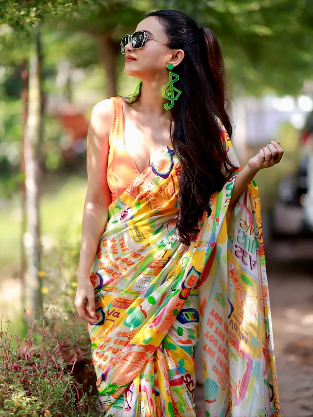 পপ-আর্ট শাড়িতে মনামীর রঙিন। শাড়ির বেজ সাদা হলেও ক্যানভাস জুড়ে ছড়িয়ে আছে উজ্জ্বল কমলা, হলুদ, সবুজ ও লালের দৃষ্টিনন্দন নকশা। জুটি হয়েছে বোল্ড কমলা স্লিভলেস ব্লাউজ। সবচেয়ে নজরকাড়া অনুষঙ্গ অবশ্যই নিয়ন সবুজ মিউজিক্যাল নোট আকৃতির স্টেটমেন্ট দুল। যারা শাড়িতে একটু এক্সপেরিমেন্টাল, আধুনিক আমেজ খুঁজছেন, তাদের জন্য মনামীর এই লুক দারুণ অনুপ্রেরণা।