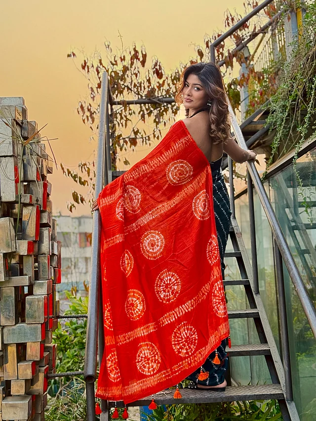 শাড়ির গাঢ় টিল রঙের জমিনে সাদা টাই-ডাই প্যাটার্ন, সঙ্গে কনট্রাস্টিং উজ্জ্বল কমলা আঁচল পুরো লুকটিকে করেছে নজরকাড়া। শাড়িটি ফ্যাশন ব্র্যান্ড রেড বাটন থেকে নেওয়া