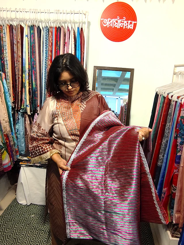 সাবেকি ঐতিহ্যের ছোঁয়ায় পরম্পরা সিল্কের আনারকলি শাড়ি নিয়ে এসেছে ভারমিলিয়ন । শাড়িটি যেন পুরোনো দিনের আভিজাত্যকে নতুন করে হাজির করেছে। জড়িসুতার সূক্ষ্ম কাজ করা লাল রঙের শাড়িটি প্রথম দেখাতেই নজর কাড়বে মেলায় । পাশাপাশি আরেকটি ভিন্ন রঙেও পাওয়া যাচ্ছে শাড়িটি