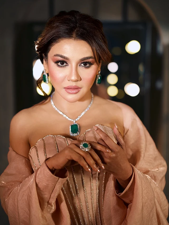 বড় এমেরাল্ড বসানো সাদা পাথরের নেকলেস, দুল ও আংটি দেখা যাচ্ছে। ন্যুড গোলাপি লিপস আর সফট গ্ল্যাম ফিনিশের মেকওভারে গোলাপির টাচ। কাজল-মাসকারায় চোখের সাজে স্মোকির বদলে ফ্রেশ আমেজ
