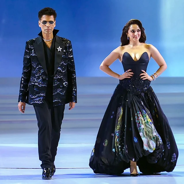 সিঙ্গেল ল্যাপেল, মিল্কি ওয়ে এফেক্টের এমবেলিশ করা স্যুট জ্যাকেটের সঙ্গে ল্যাপেলের তারা আর কালো শার্টের উঁচু কলার নজর কাড়ছে করণ জোহরের স্ট্রেট কাট কালো টাউজার্সের সঙ্গে। পায়ে গ্লসি কালো ড্রেস শুজ। গলায় রূপালি চেন আর চোখে কালো শেডস