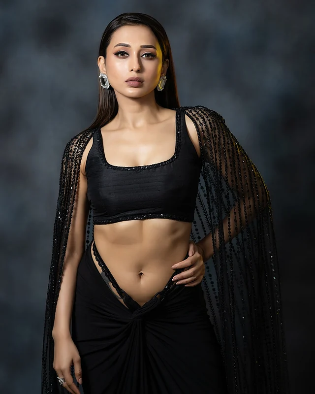 অল ব্ল্যাক এই লুকে মিমি চোখ ধাঁধাচ্ছেন একেবারে। পরেছেন কালো ব্রালেট ও লো রাইজ স্কার্টের সঙ্গে উইংড কেপ