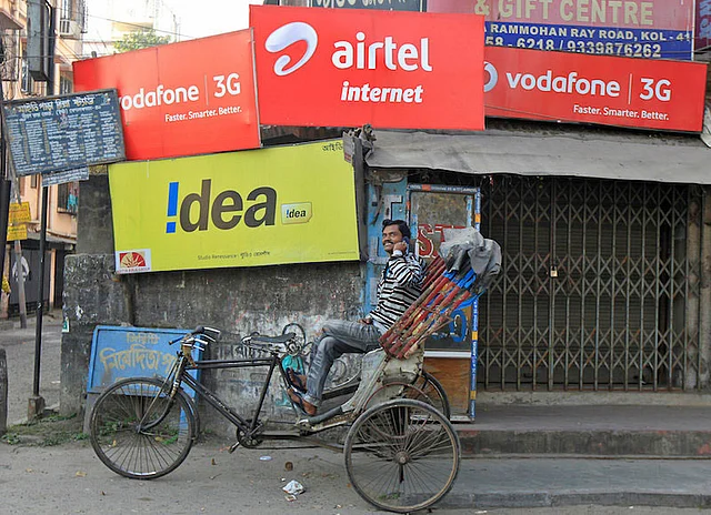 A rickshaw puller speaks on his mobile phone as he waits for customers in front of advertisement billboards belonging to telecom companies in Kolkata. Reuters file photo