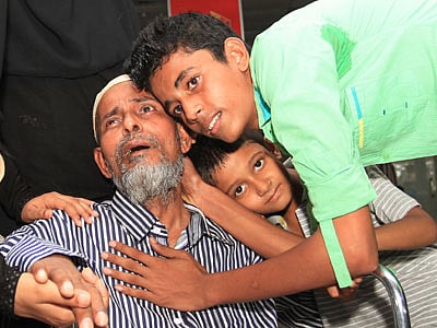বাবা পক্ষাঘাতগ্রস্ত। তবুও তো দেশে ফিরেছেন। সন্তানেরা তাতেই খুশি। ওমান থেকে দেশে ফেরার পর নাজমুল হককে জড়িয়ে ধরে আছে তাঁর দুই ছেলে। গতকাল বিমানবন্দর থেকে তোলা l ছবি: প্রথম আলো