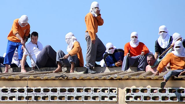 ব্রাজিলের পারানা রাজ্যে কারাগারের ছাদে দুই জিম্মিসহ মুখবাঁধা কয়েদিরা। ২৫ আগস্ট তোলা ছবিটি আজ প্রকাশ করা হয়েছে। কারাগারে সুযোগ-সুবিধা বাড়ানোর দাবিতে দাঙ্গায় লিপ্ত হয়েছে তারা। সহবন্দীদের হাতে খুন হয়েছে চারজন। জিম্মি করা হয়েছে দুই কারারক্ষীকে। ছবি: এএফপি