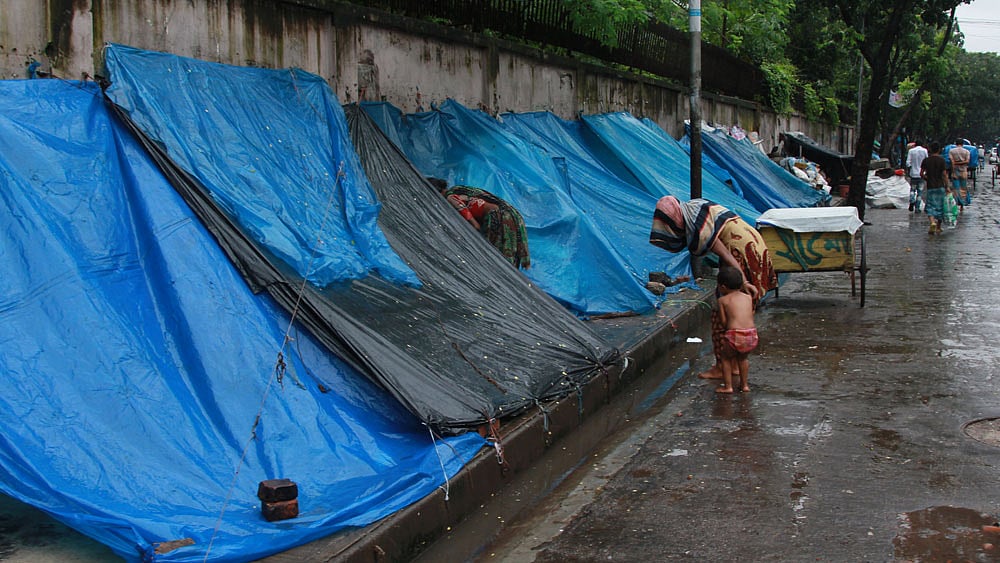 বৃষ্টিতে ফুটপাতে প্লাস্টিকের ঢালু ছাউনির নিচে আশ্রয় নিয়েছে ছিন্নমূল মানুষ। ছবিটি আজ বেলা সাড়ে ১১টার দিকে রাজধানীর পলাশী মোড়-সংলগ্ন এলাকা থেকে তোলা। ছবি: জাহিদুল করিম