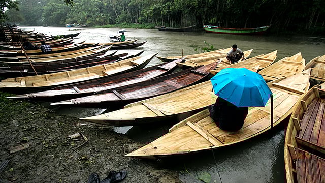 বৃষ্টিতে নৌকা বিক্রির জন্য ছাতা মাথায় বসে আছেন বিক্রেতা। ছবিটি শুক্রবার বরিশাল থেকে তোলা। ছবি: সাইয়ান, বরিশাল