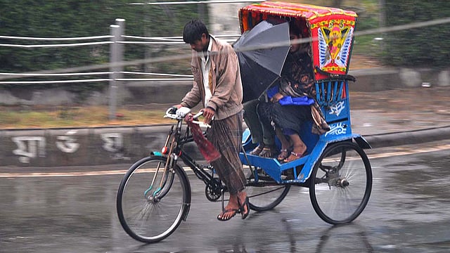 শীতকাল হওয়ায় রিকশাচালকেরা প্লাস্টিকের পর্দা নিয়ে বের হন না। তাই হঠাৎ​ বৃষ্টিতে ছাতা দিয়ে নিজেদের রক্ষা করার চেষ্টা করেছেন যাত্রীরা। ছবিটি শহরের একটি রাস্তা থেকে তোলা। ছবি: প্রথম আলো