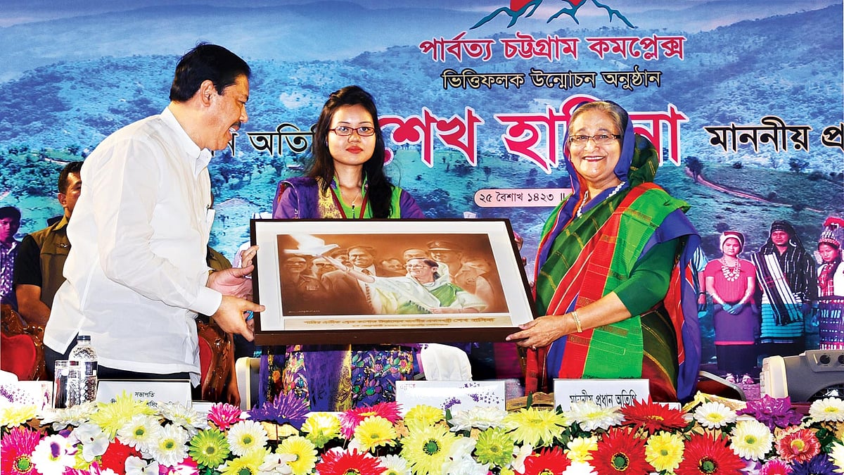 রাজধানীর বেইলি রোডে গতকাল পার্বত্য চট্টগ্রাম কমপ্লেক্সের ভিত্তিফলক উন্মোচন অনুষ্ঠানে প্রধানমন্ত্রী শেখ হাসিনার হাতে উপহার হিসেবে একটি ছবি তুলে দেন পার্বত্য চট্টগ্রাম-বিষয়ক মন্ত্রণালয়ের প্রতিমন্ত্রী বীর বাহাদুর উ শৈ সিং l ছবি: বাসস