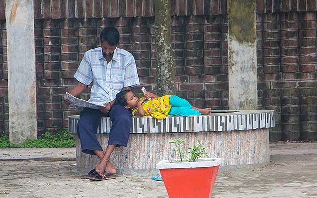 বাবা পত্রিকা পড়ছেন। তাঁর কোলে মাথা রেখে মেয়ে মোবাইল ফোনে গেমস খেলছে। ছবিটি আজ শুক্রবার খুলনা মেডিকেল কলেজ হাসপাতাল-সংলগ্ন এলাকা থেকে তোলা। ছবি: মো. সাদ্দাম হোসেন