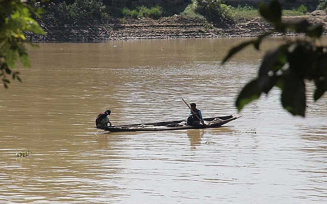 সিলেটের সুরমা নদী। সেখানে নৌকায় করে জাল দিয়ে মাছ ধরছেন দুই ব্যক্তি। ছবিটি নগরের কাজিরবাজার এলাকা থেকে আজ শনিবার দুপুরে তোলা। ছবি: আনিস মাহমুদ