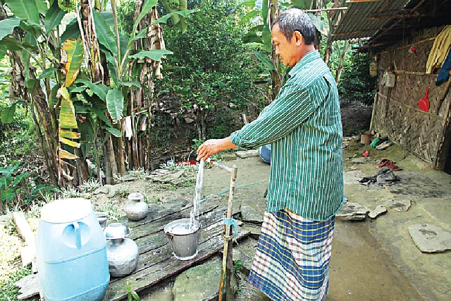 নিজের বাড়ির আঙিনায় কল থেকে পানি সংগ্রহ করছেন চৈ ছড়ি মোনপাড়ার এক বাসিন্দা l প্রথম আলো