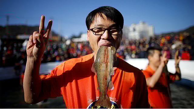 আইস ফেস্টিভ্যালে হাত দিয়ে মাছ ধরারও ছিল আয়োজন। সেখানে একজন সফল হয়ে ‘ভি’ চিহ্ন দেখাচ্ছেন। ছবি: রয়টার্স