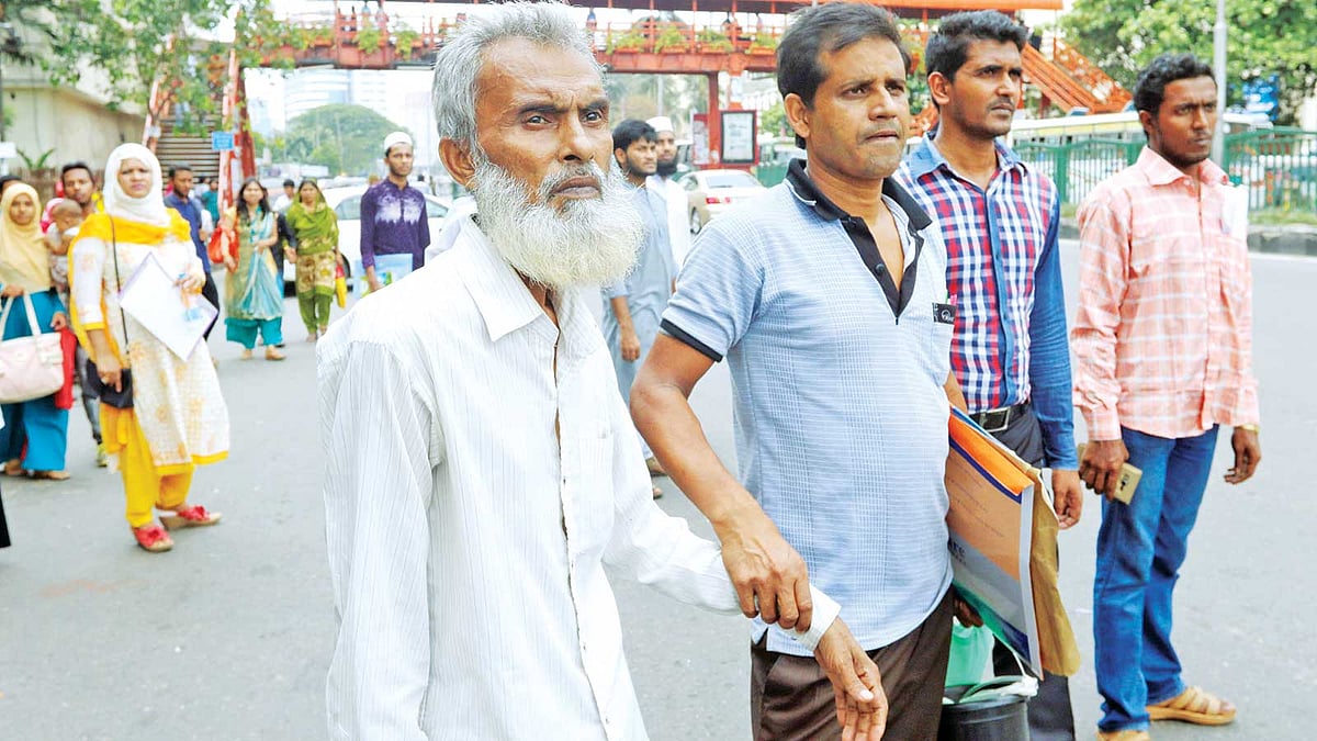ক্যানসারের রোগী সুলতান মিয়াকে (বাঁয়ে) নিয়ে মহাখালীর ক্যানসার হাসপাতালে যেতে প্রায় এক ঘণ্টা শাহবাগ মোড়ে বাসের অপেক্ষায় দাঁড়িয়ে ছিলেন হারুন উর রশিদ। এ সময় বাসের অপেক্ষায় আরও অনেকেই সেখানে দাঁড়িয়ে ছিলেন। ছবিটি গতকাল দুপুরে তোলা l আবদুস সালাম