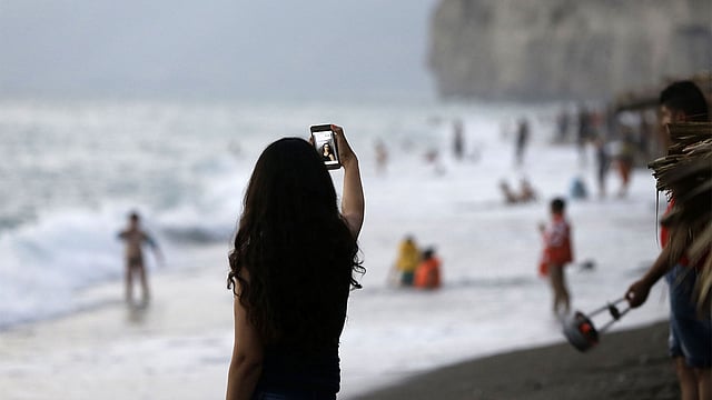 সমুদ্রের উত্তাল ঢেউয়ের পাশে দাঁড়িয়ে জীবনের ঝুঁকি নিয়ে সেলফি তুলছেন এক তরুণী। প্রতীকী ছবি: এএফপি