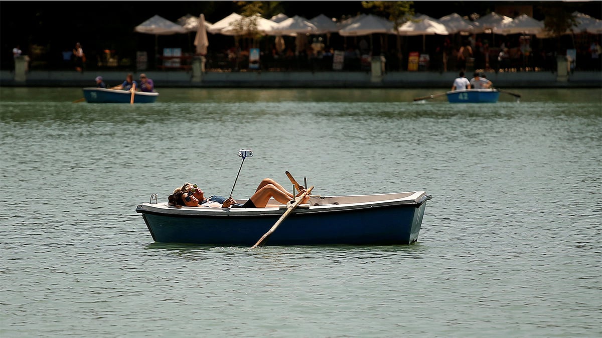 জলাশয়ের মাঝে নৌকায় শুয়ে সেলফি তুলছেন দুই নারী। প্রতীকী ছবি: রয়টার্স