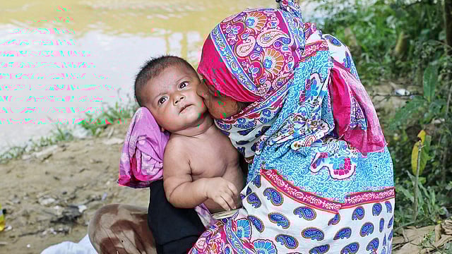 গরমে অতিষ্ঠ এক রোহিঙ্গা নারী তাঁর সন্তানকে গাছের ছায়ায় আদর করছেন। ছবিটি গতকাল সকালে টেকনাফের তাজনিমারঘোনার অস্থায়ী আশ্রয় শিবির থেকে তোলা l সাবিনা ইয়াসমিন