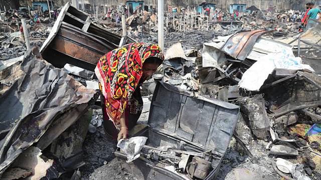 রাজধানীর মিরপুর ১২ নম্বরের ইলিয়াস মোল্লা বস্তিতে ভয়াবহ আগুনে পুড়ে যাওয়া জিনিসপত্রের মধ্যে এক নারীর খোঁজাখুঁজি। প্রথম আলো ফাইল ছবি।