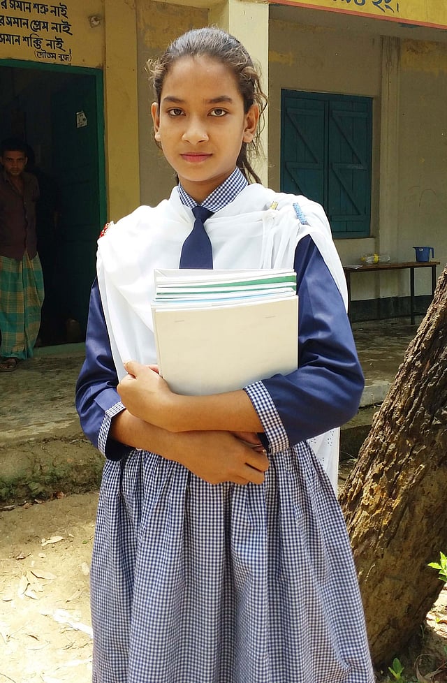নিজ বিদ্যালয়ের সামনে বই হাতে দাঁড়িয়ে শরমিন আক্তার। সম্প্রতি চট্টগ্রামের লোহাগাড়া উপজেলা সদরের ফয়েজ শফি সরকারি প্রাথমিক বিদ্যালয়ে।  প্রথম আলো