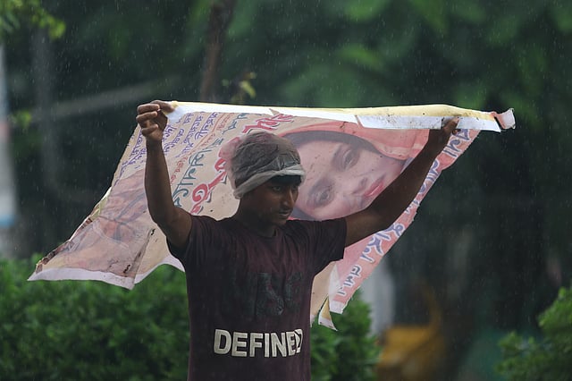 রাজধানীতে বিকেলের বৃষ্টি থেকে বাঁচতে মাথার ওপর বড় পোস্টার মেলে ধরে এক যুবক। রাজু ভাস্কর্য এলাকা, ঢাকা বিশ্ববিদ্যালয় এলাকা, ২৬ জুলাই। ছবি: আবদুস সালাম