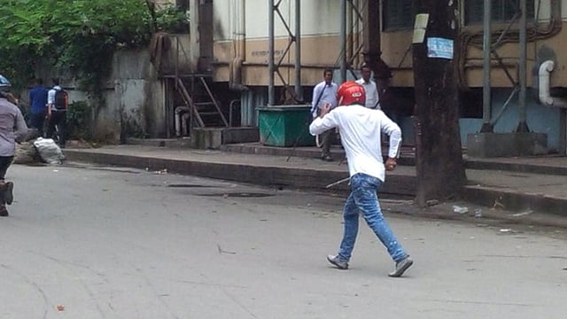 লাঠি হাতে, হেলমেট পরে শিক্ষার্থীদের দিকে তেড়ে যাচ্ছে এক যুবক।