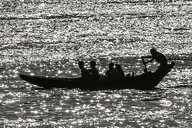 পড়ন্ত বিকেলে রৌদ্রোজ্জ্বল ঢেউয়ের তালে যাত্রীসমেত মাঝি।