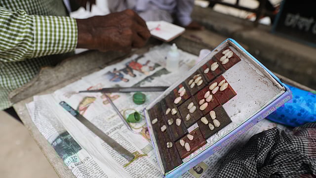 রাস্তার পাশের ড্রেনের ওপর পাটাতন দিয়ে দোকান খুলে বসছেন তাঁরা। টেবিলে সাজিয়ে রেখেছেন কিছু পুরোনো যন্ত্রপাতি ও তরলে ভরা কয়েকটি বোতল। দোকানে এইগুলোর সঙ্গে রাখা হয়েছে নানা আকারের দাঁত।