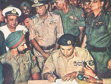 ১৯৭১ সালের ১৬ ডিসেম্বর বিকেল সাড়ে চারটায় তৎকালীন রেসকোর্স ময়দানে আত্মসমর্পণ দলিলে স্বাক্ষর করছেন নিয়াজি। পাশে বসে আছেন অরোরা। ছবি: সংগৃহীত