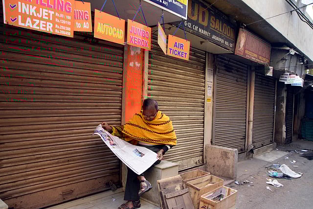দোকানপাট বন্ধ থাকায় অলস সময় পেয়ে পত্রিকা পড়ায় ব্যস্ত এক ব্যক্তি। যাদবপুর, পশ্চিমবঙ্গ, ভারত। ছবি: ভাস্কর মুখার্জি