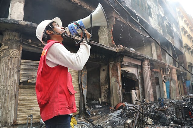 পোড়া ধ্বংসস্তূপে দাঁড়িয়ে কী যেন বলছেন এক উদ্ধারকর্মী। চকবাজার, ঢাকা, ২১ ফেব্রুয়ারি। ছবি: আবদুস সালাম