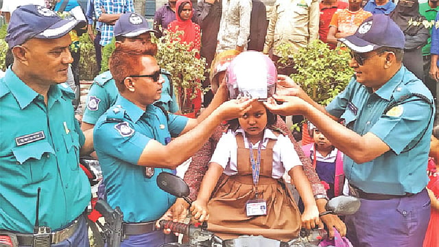 স্কুলগামী শিশু শিক্ষার্থীর মাথায় হেলমেট পড়িয়ে দিচ্ছেন ডিএমপির ট্রাফিক বিভাগের কর্মকর্তারা।