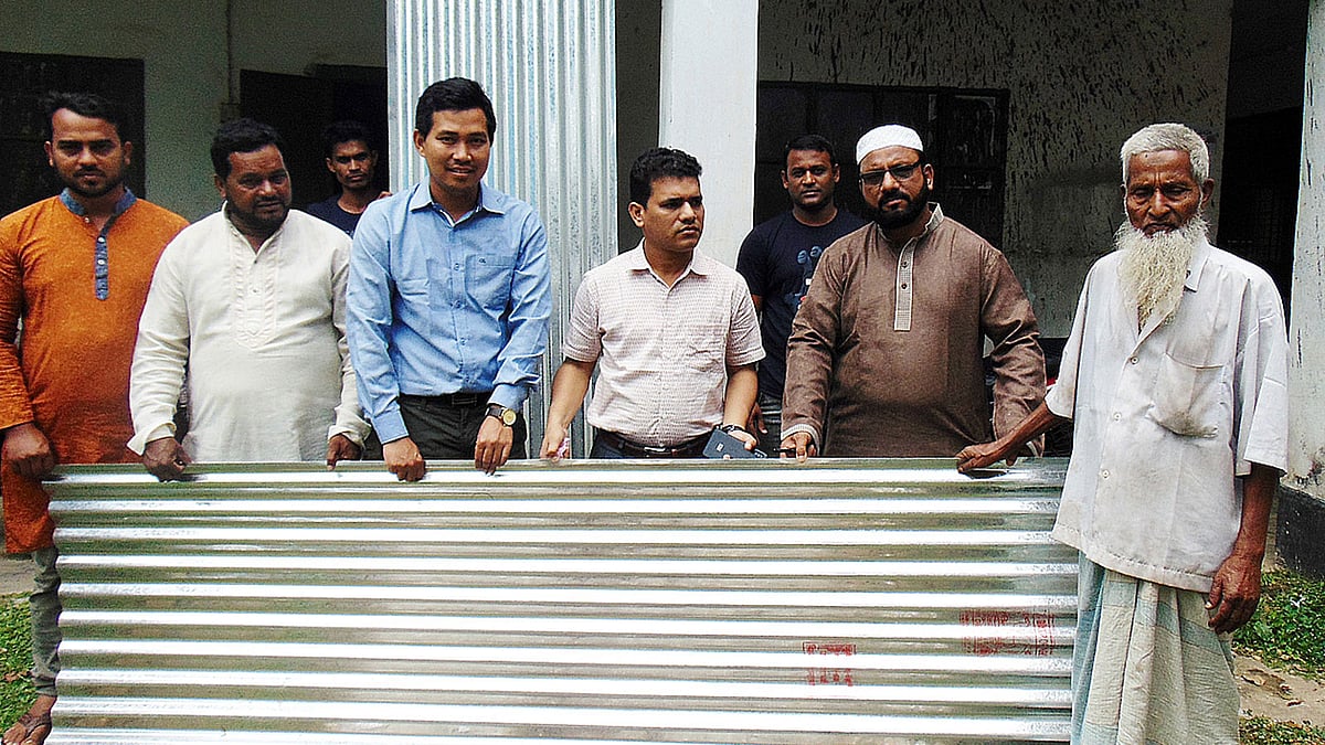 বিধ্বস্ত ঘর মেরামতের জন্য বৃদ্ধের হাতে টিন তুলে দেন ইউএনও মাসুদুর রহমান। ছবি: প্রথম আলো