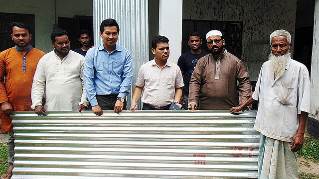 বিধ্বস্ত ঘর মেরামতের জন্য বৃদ্ধের হাতে টিন তুলে দেন ইউএনও মাসুদুর রহমান। ছবি: প্রথম আলো