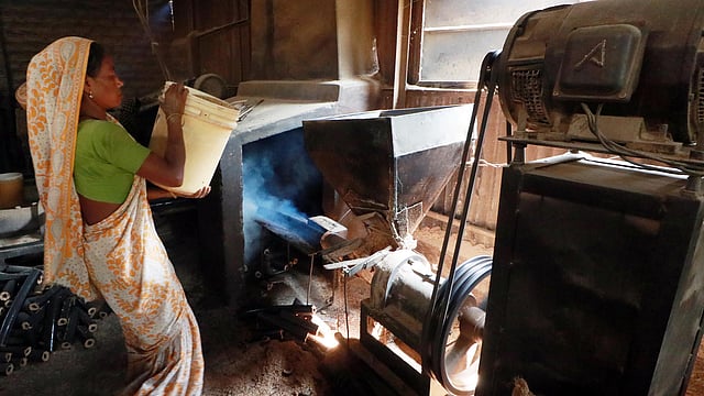 মেশিনে তুষ ঠেলে দিচ্ছেন এক নারী শ্রমিক। তুষ থেকে তৈরি হবে লাকড়ি