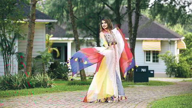 হাতের কাজ, টার্সেলের ব্যবহার আর উজ্জ্বল রং মসলিনের এই পোশাকে নিয়ে এসেছে আভিজাত্য। সামনে ফাড়া দেওয়া ম্যাক্সি পোশাকটির ওড়নাটিতেও টাই-ডাইয়ের মাধ্যমে বিভিন্ন শেড আনা হয়েছে। সঙ্গে সোজা কাটের সাদা প্যান্ট।  পোশাক: হুমায়রা খান