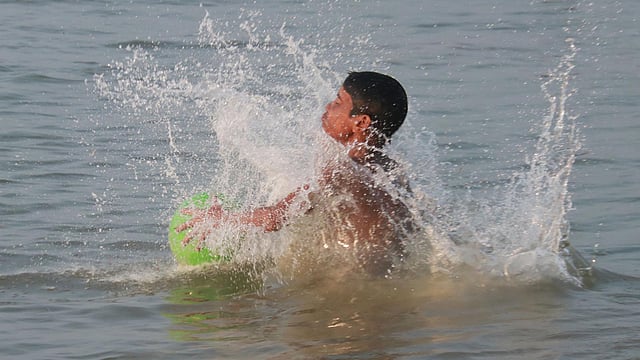বল নিয়ে পানিতে খেলছে এক কিশোর