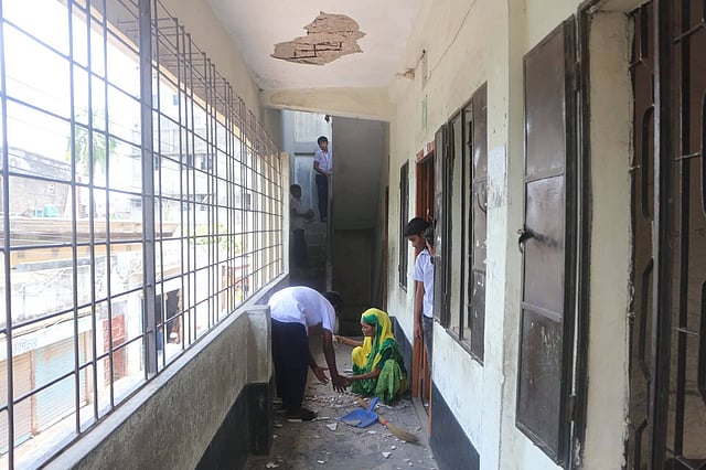 ক্লাস চলাকালে বারান্দার সিলিংয়ের পলেস্তারা খসে পড়েছে। শিক্ষার্থী ও কর্মী পলেস্তারা পরিষ্কার করছেন। লক্ষ্মীনারায়ণ সরকারি প্রাথমিক বিদ্যালয়, দেওভোগ আখড়া, নারায়ণগঞ্জ, ২৪ জুন। ছবি: দিনার মাহমুদ
