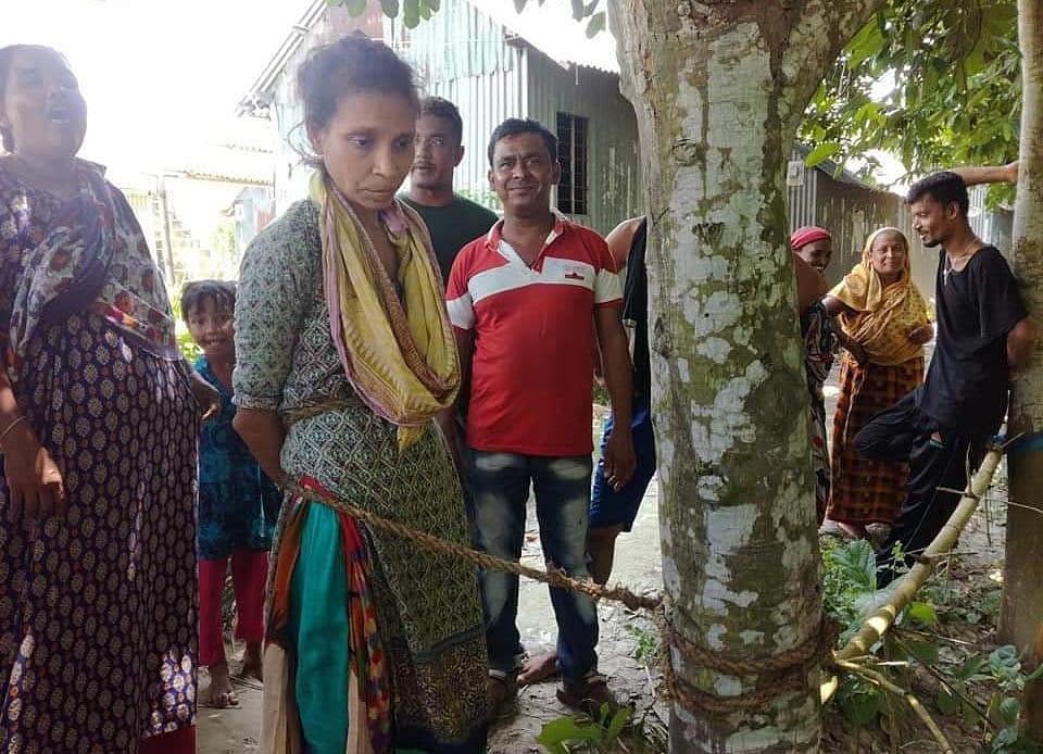 ছেলেধরা সন্দেহে মানসিক ভারসাম্যহীন নারীকে গাছে বেঁধে নির্যাতন করেছেন স্থানীয় লোকজন। পরে পুলিশ গিয়ে তাঁকে উদ্ধার করে। মাদারীপুর, ঢাকা, ২২ জুলাই। ছবি: প্রথম আলো