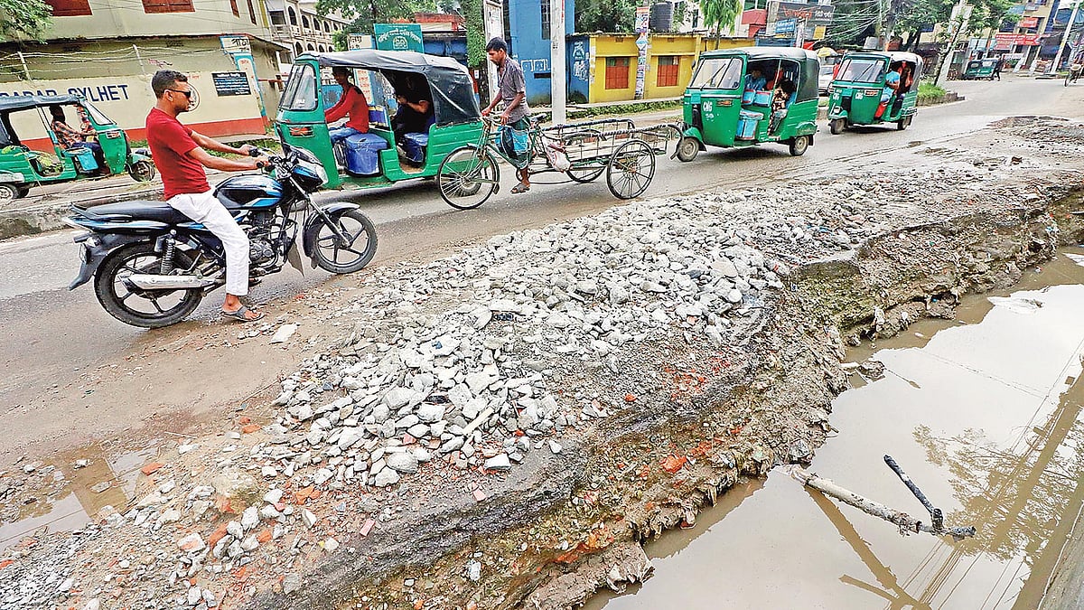 নর্দমার পানির স্রোতে ভেঙে গেছে সড়ক। ভাঙা সড়কে ঝুঁকি নিয়ে চলছে যানবাহন। গতকাল বিকেলে সিলেট সুনামগঞ্জ সড়কের পাঠানটুলা এলাকায়। ছবি: প্রথম আলো